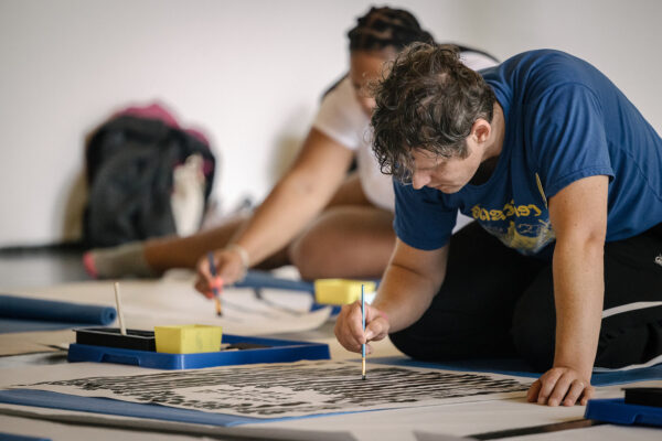 Two people work on painting on large white posterboards on the floor