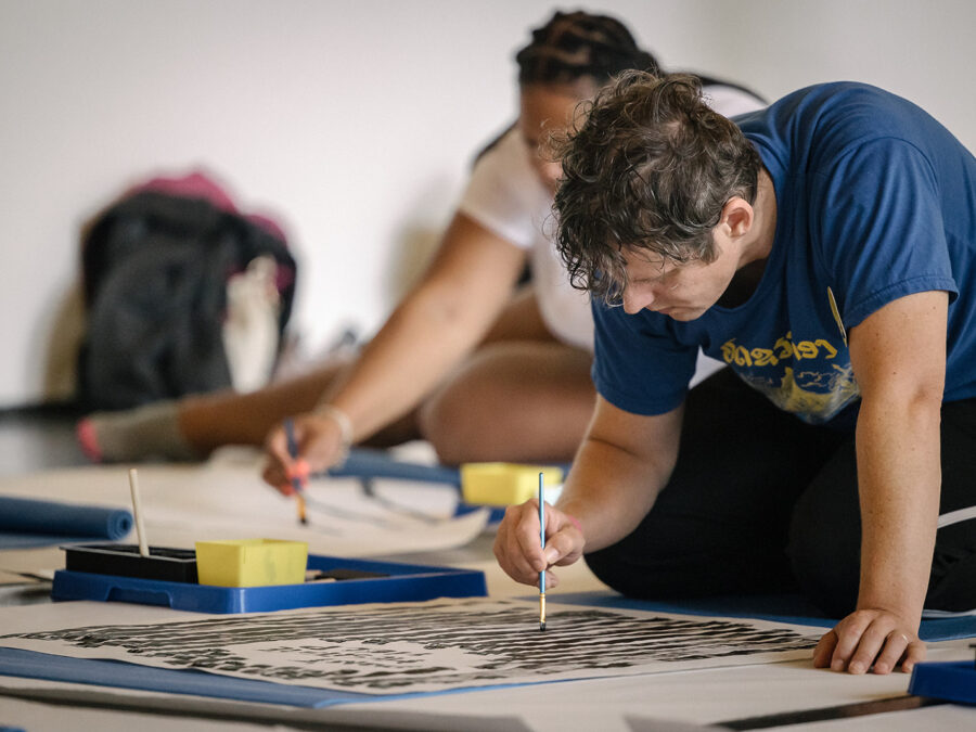 Two people work on painting on large white posterboards on the floor
