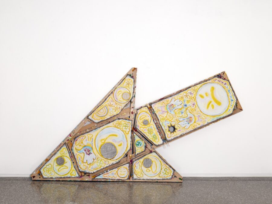 Painted emojis against a yellow background on unusually shaped canvases that form an arrow resting on the floor against a white wall