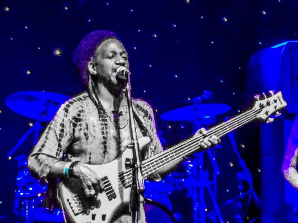 A guitarist sings into the microphone in this edited image where they are in black in white and the background is an indigo blue