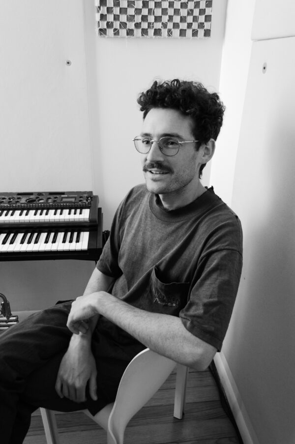 Black and white image of a mustached person sitting next to a two-tiered keyboard