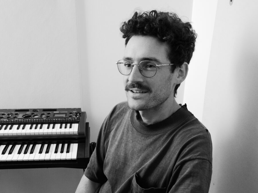 Black and white image of a mustached person sitting next to a two-tiered keyboard