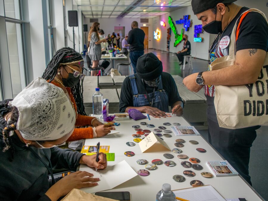 A group of people write at a tables filled with pins