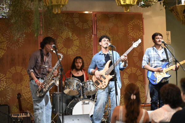 Band of teens plays instruments and performs on a stage.