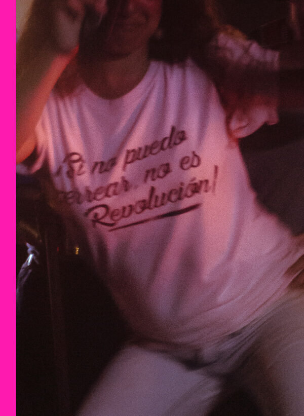 Person dancing energetically in a crowd, wearing a white t-shirt with the text 'En la muela de atrás no es revolución' (which translates to 