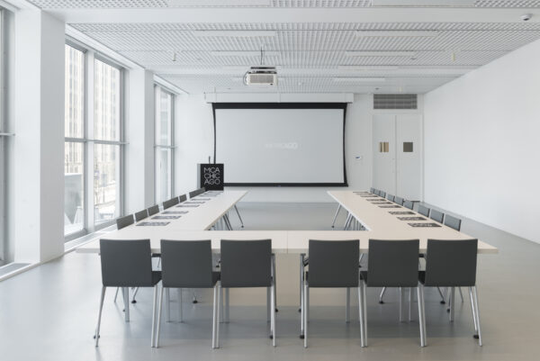 A white conference venue set up with tables and chairs arranged in a u-shape