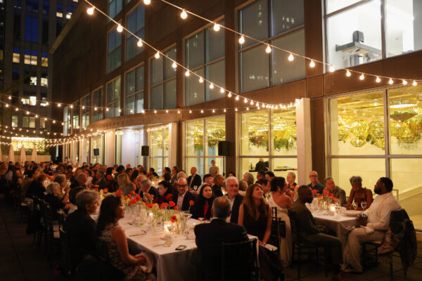 Two long tables filled with people outside beneath string lights creating an elegant feel