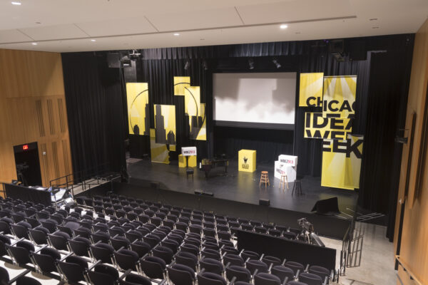 Banners, a screen, and a podium are set up in a theater for Chicago Ideas Week
