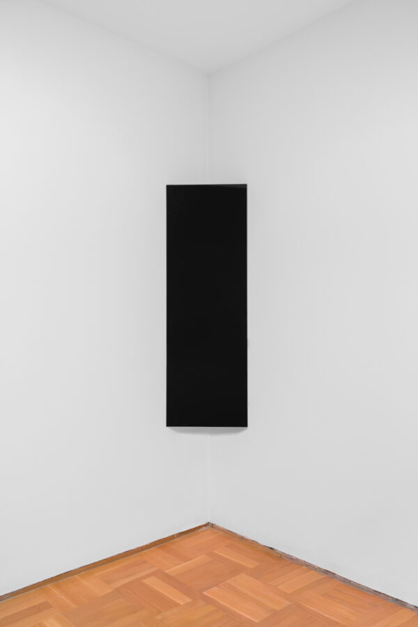 A stark black rectangle hung vertically in the corner of a white-walled room.