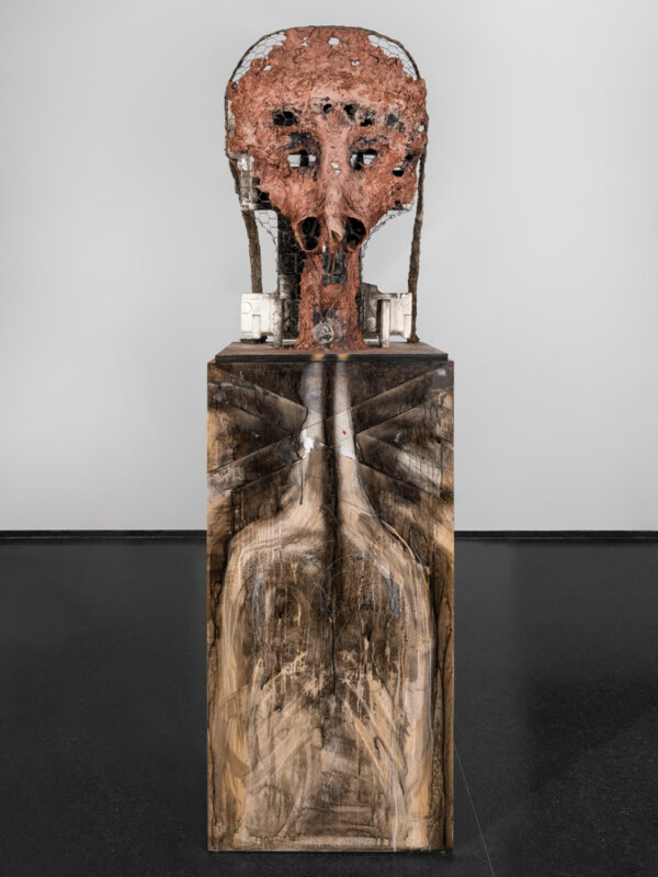 A sculpture resembling a human with head-like object on top of a vertical box that has been painted black and white