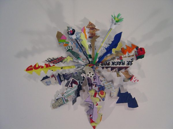 Colorful paper cut into zig-zags form a firework shaped sculpture hung on a wall