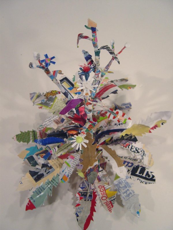 Colorful cut paper shapes with zig-zag edges form are bundled in sculpture hung on a wall