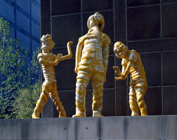 Three larger-than-life yellow figures face each other in an outdoor installation