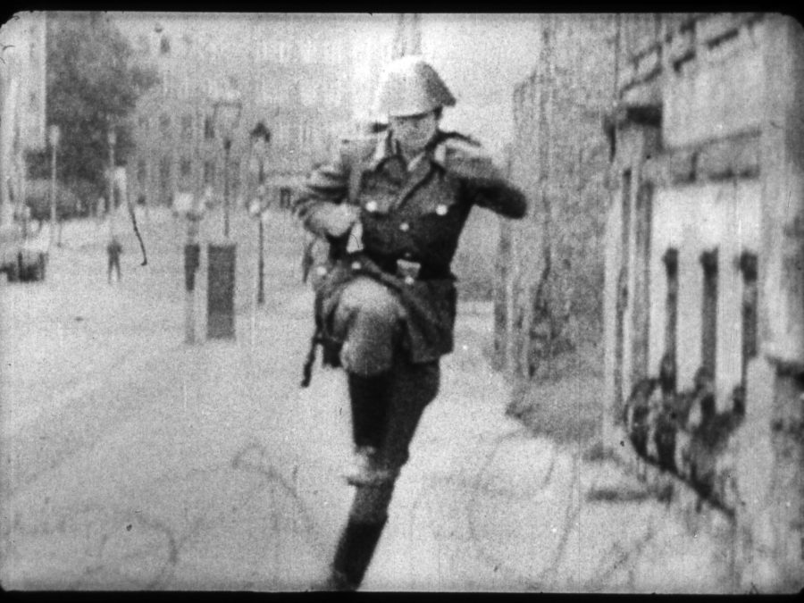 Archival image of a person dressed in a vintage military uniform and helmet running down a sidewalk