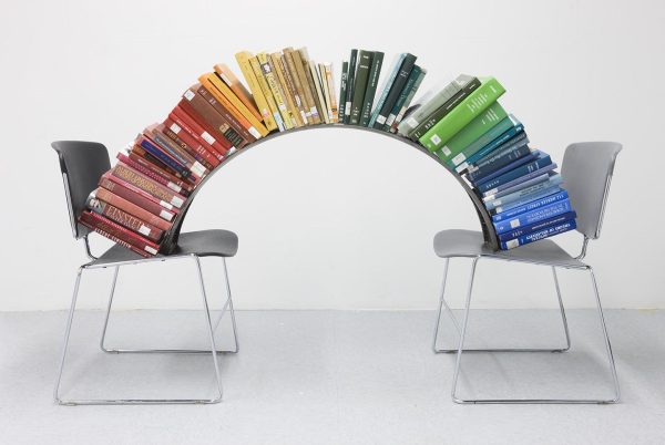 A colorful, curved stack of books reaches from one chair to another.