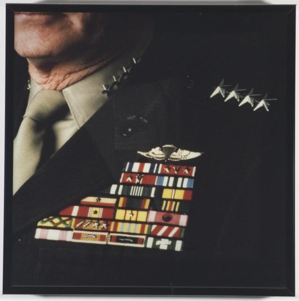 A close-up image shows an older person wearing a military uniform with many brightly colored badges on the lapel of the jacket.