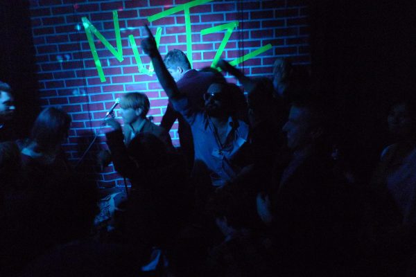 Young people dance in dark room with a single spotlight near a brick wall with the word 