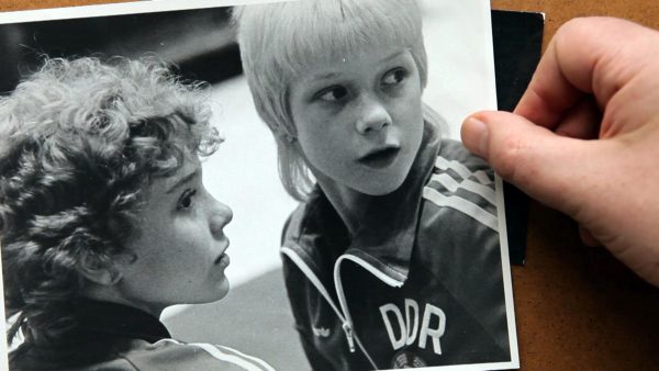 A light skinned right hand holds a black and white photo of two kids looking off at something to their left