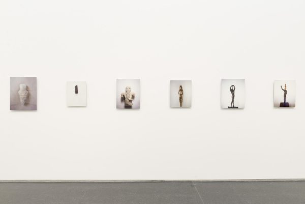 Six photographs are hung on a white wall. Each photograph is a picture of a different sculpture from various civilizations throughout history.