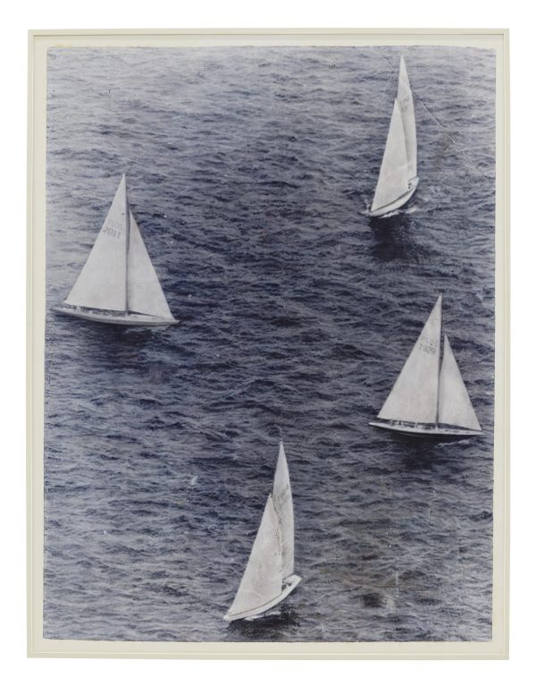 A faded black-and-white photograph shows four sailboats sailing in close proximity.
