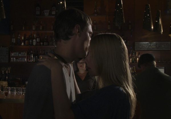 Two people stand very close together in a dark bar setting