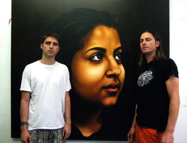 Two people posing next to a larger-than-life painting of a female-presenting person