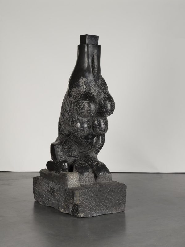 A black stone statue of a headless, dog-like animal with four breasts