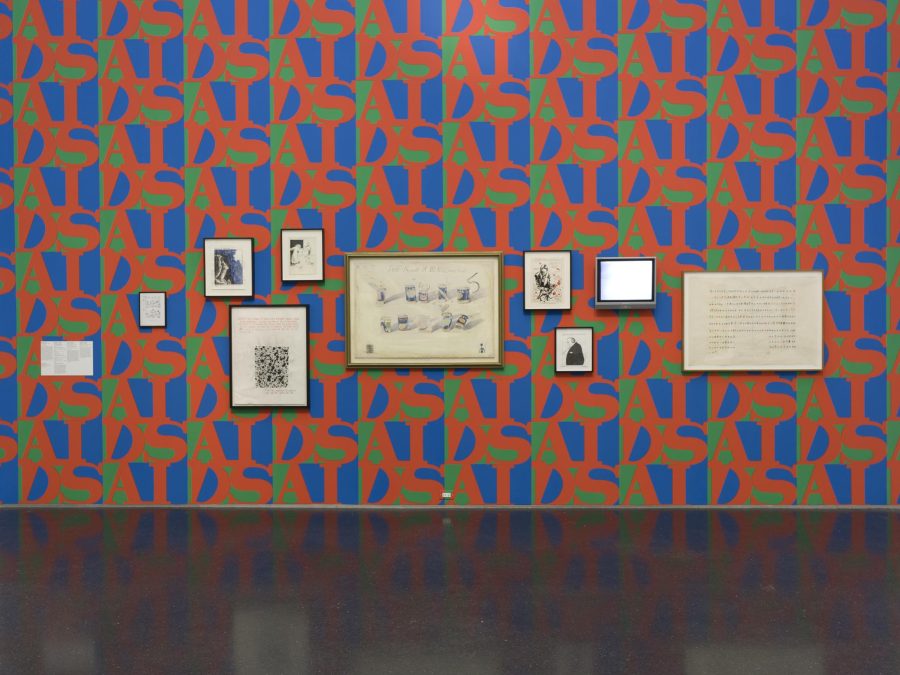 Artworks of varying sizes hung on a wall featuring AIDS patterned wallpaper