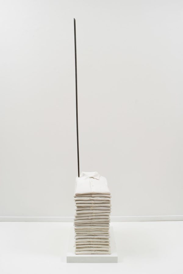 A stack of folded white polos is pierced by a vertical metal rod.
