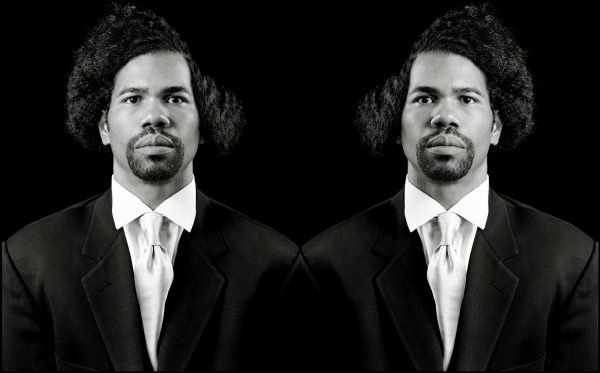 Black and white mirrored portrait of a man with a goatee in a suit
