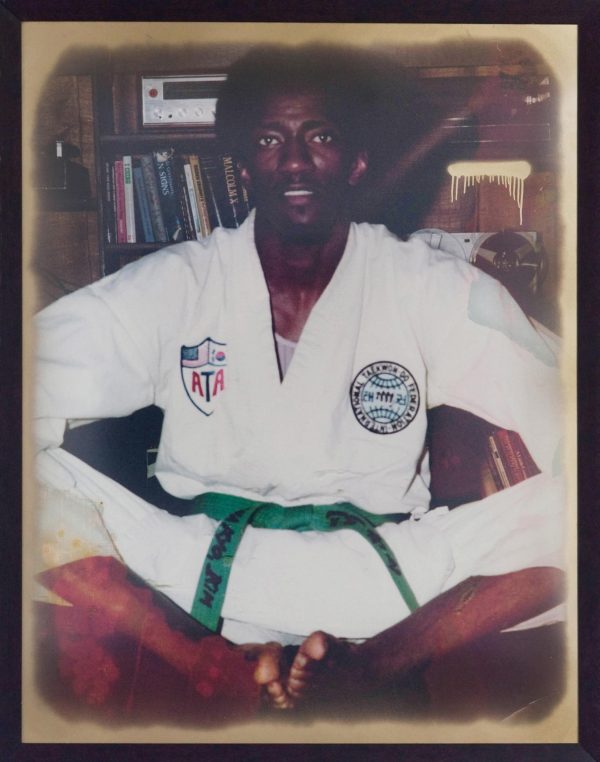 A dark-skinned person wearing a Taekwondo uniform sits on the ground.
