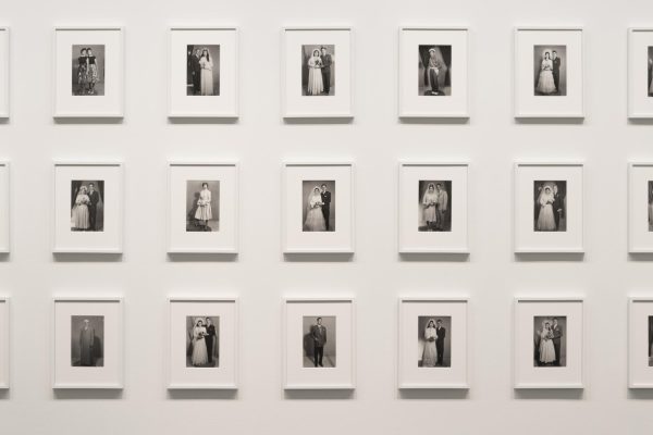 Neat rows of identically sized formal wedding portraits are matted and framed in white on a white wall.