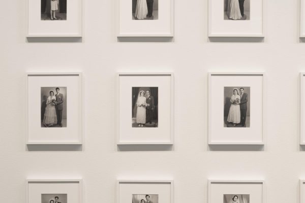 Identically sized, formal black-and-white wedding portraits are matted and framed in white, hanging in even rows on a white wall.