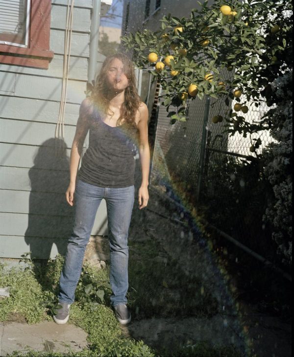 A young person is standing outdoors and spitting liquid underneath a lemon tree.
