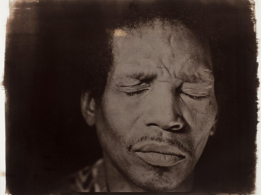 A brown-toned photograph featuring a close-up of a male-presenting person with their eyes closed