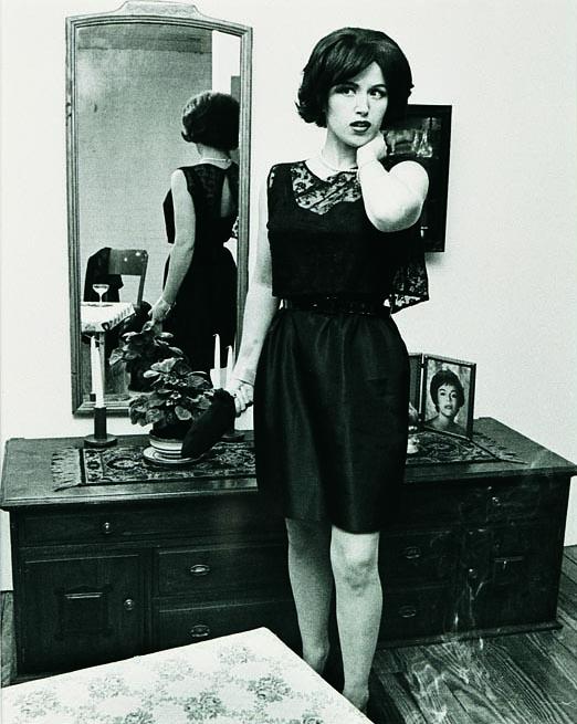 a woman stands holding an unidentifiable object looking just past the camera