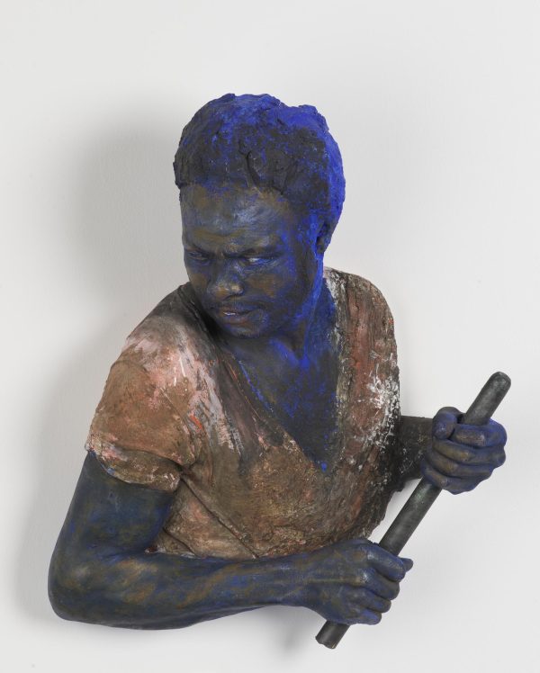 A bust of a dark-skinned person is holding a short, narrow pole while looking over their right shoulder. The bust appears to be dusted with cobalt-blue powder.