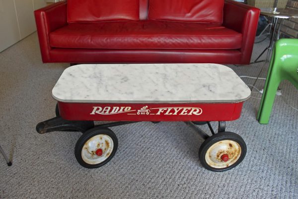 A red Radio Flyer wagon with a white marble top serves as a coffee table in a sitting room setting.