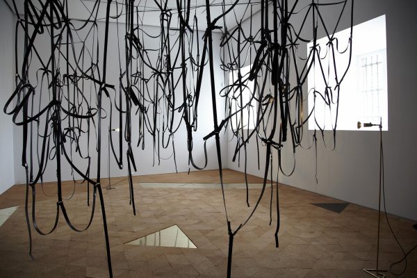 Entangled black strips of fabric hang from the ceiling in a room with shimmery triangles inlaid into the wooden floor