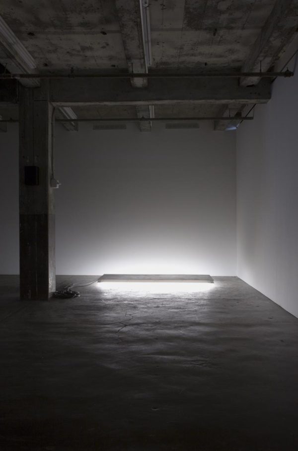In a dark room a large rectangle light on the floor casts a bright white light into the corner