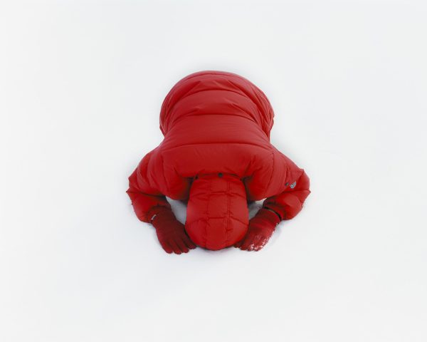 A person in a red puffy coat and red gloves bows on a snow-covered surface. Their face is not seen.