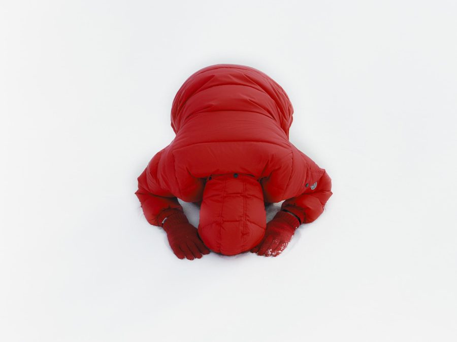 A person in a red puffy coat and red gloves bows on a snow-covered surface. Their face is not seen.