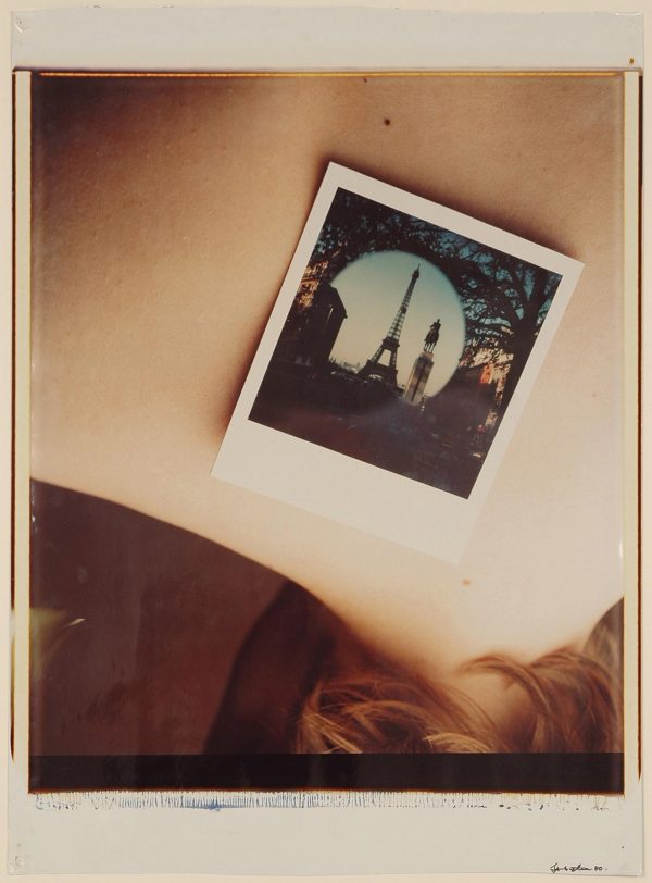A photograph of a person's back with a Polaroid picture on it of the Eiffel Tower reflected in a round mirror