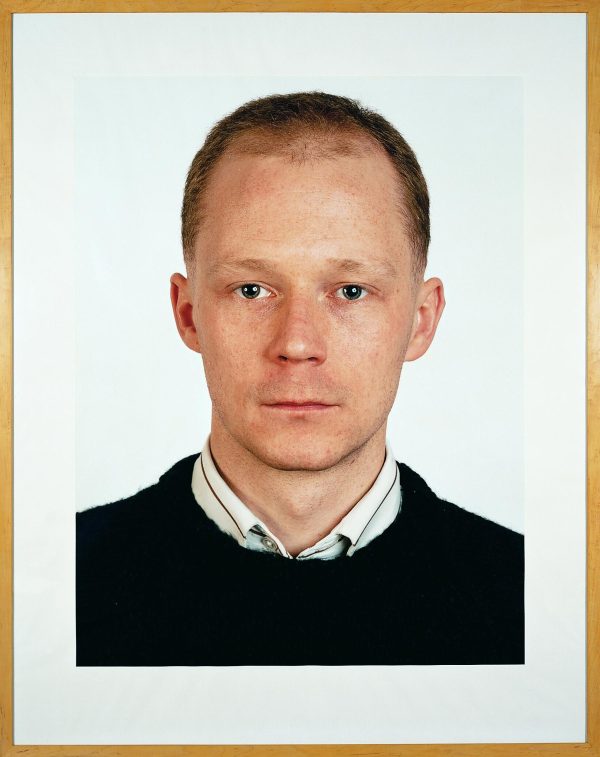 A frontal portrait features a person looking just off-camera, wearing a collared shirt under a sweater.