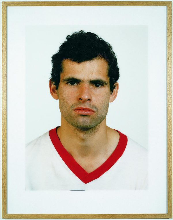 A frontal portrait features a person wearing a white shirt with a red collar.