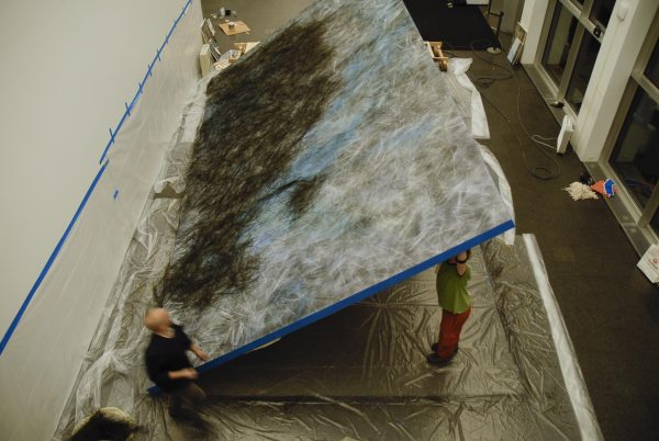 A small group of people tilt a large canvas that rests on a large plastic sheet