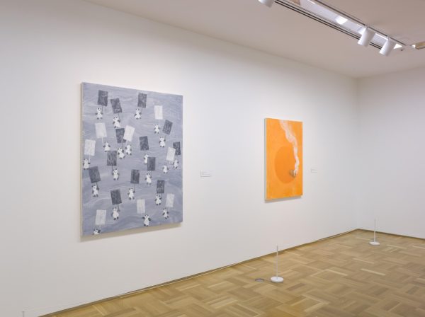 Angled view of a gallery space with two paintings hanging on the left wall