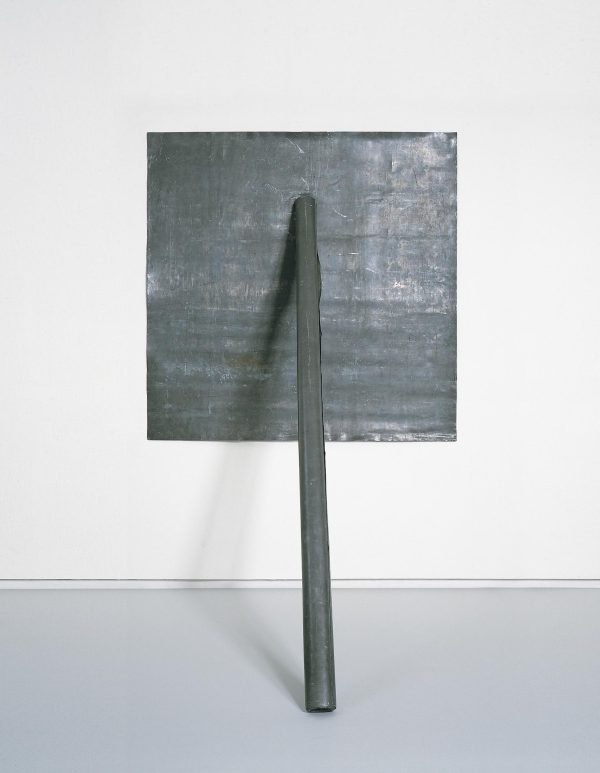 A thick metal pole rests against a metal square on a white wall
