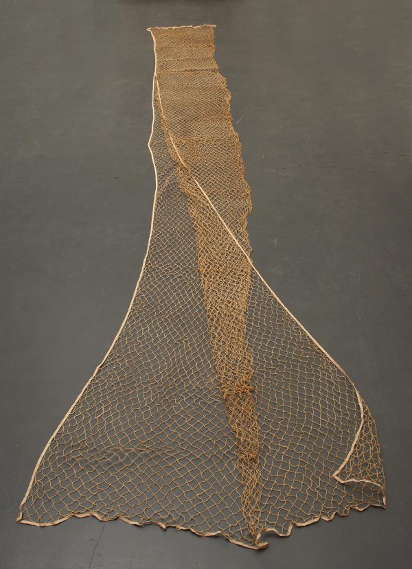 A long brown fishnet fabric on the floor. It is slowly unfolded so that the part closest to the foreground is nearly at its full width.