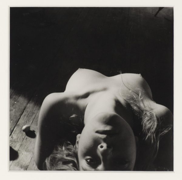 A black-and-white photograph shows a light-skinned person without a shirt on leaning backward so their face is upside down.